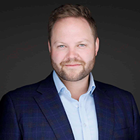 Professional headshot of a man in a blue suit and light blue shirt.