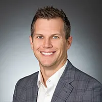 Professional headshot of a smiling man in a gray suit jacket.