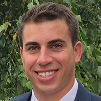 Headshot of a smiling man in a suit with a green leafy background.