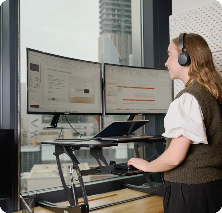 Woman using a standing desk with dual monitors in a modern office.