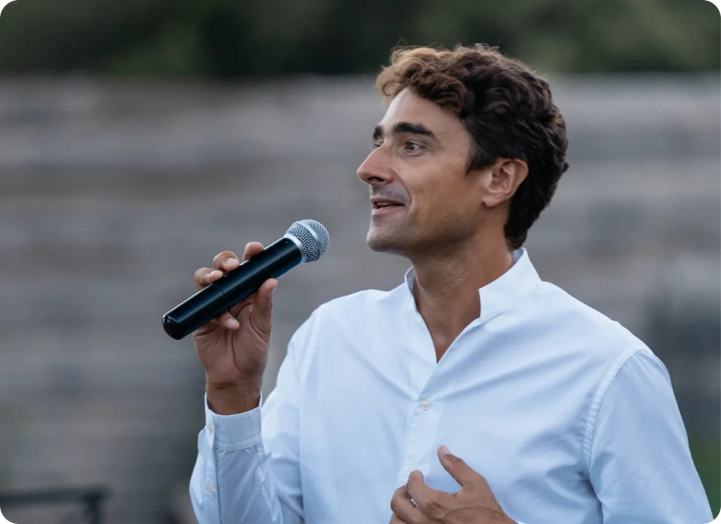 Man speaking into a microphone, possibly in an UpSlide presentation or event.