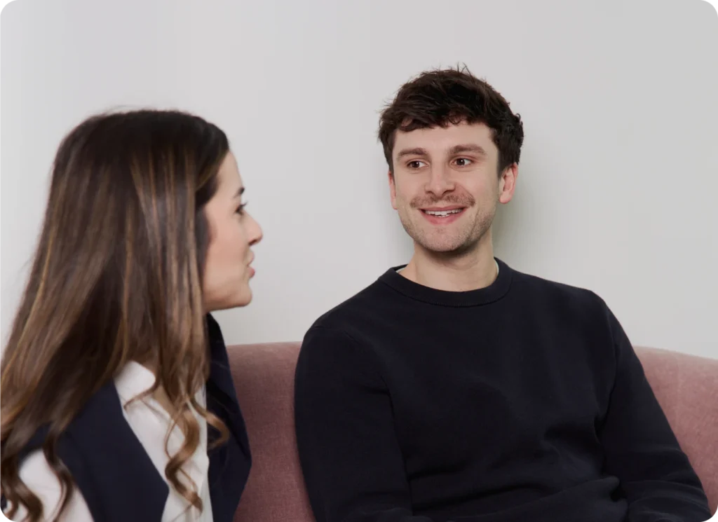Man smiling while talking to a woman on a couch