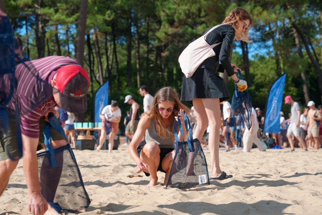 Upslide B Corp volunteers clean up a sandy beach, collecting trash in blue bags.
